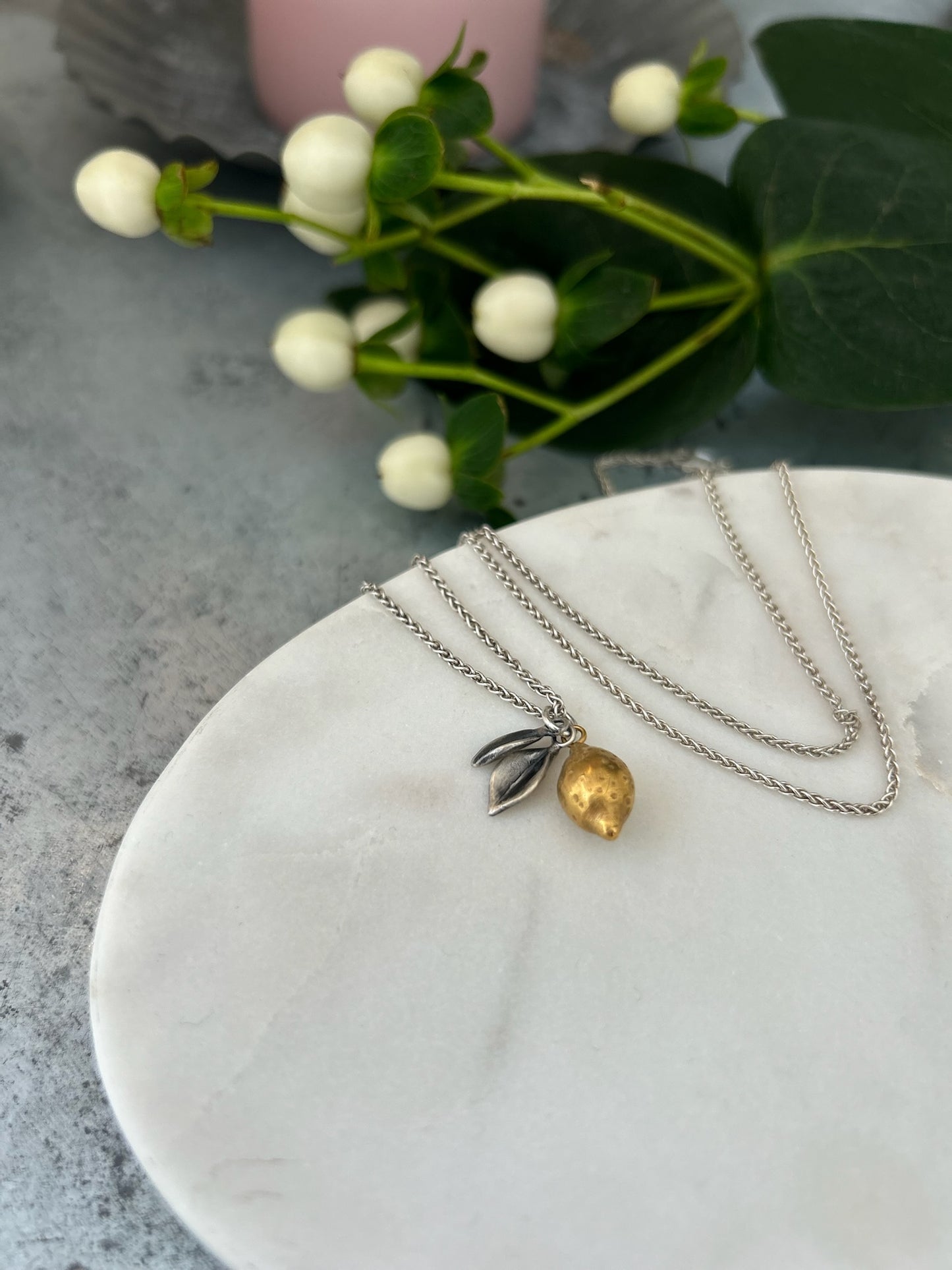 Image shows a Lemon pendant, the lemon is plated in 18ct gold with oxidised silver leaves, hanging from a silver chain.