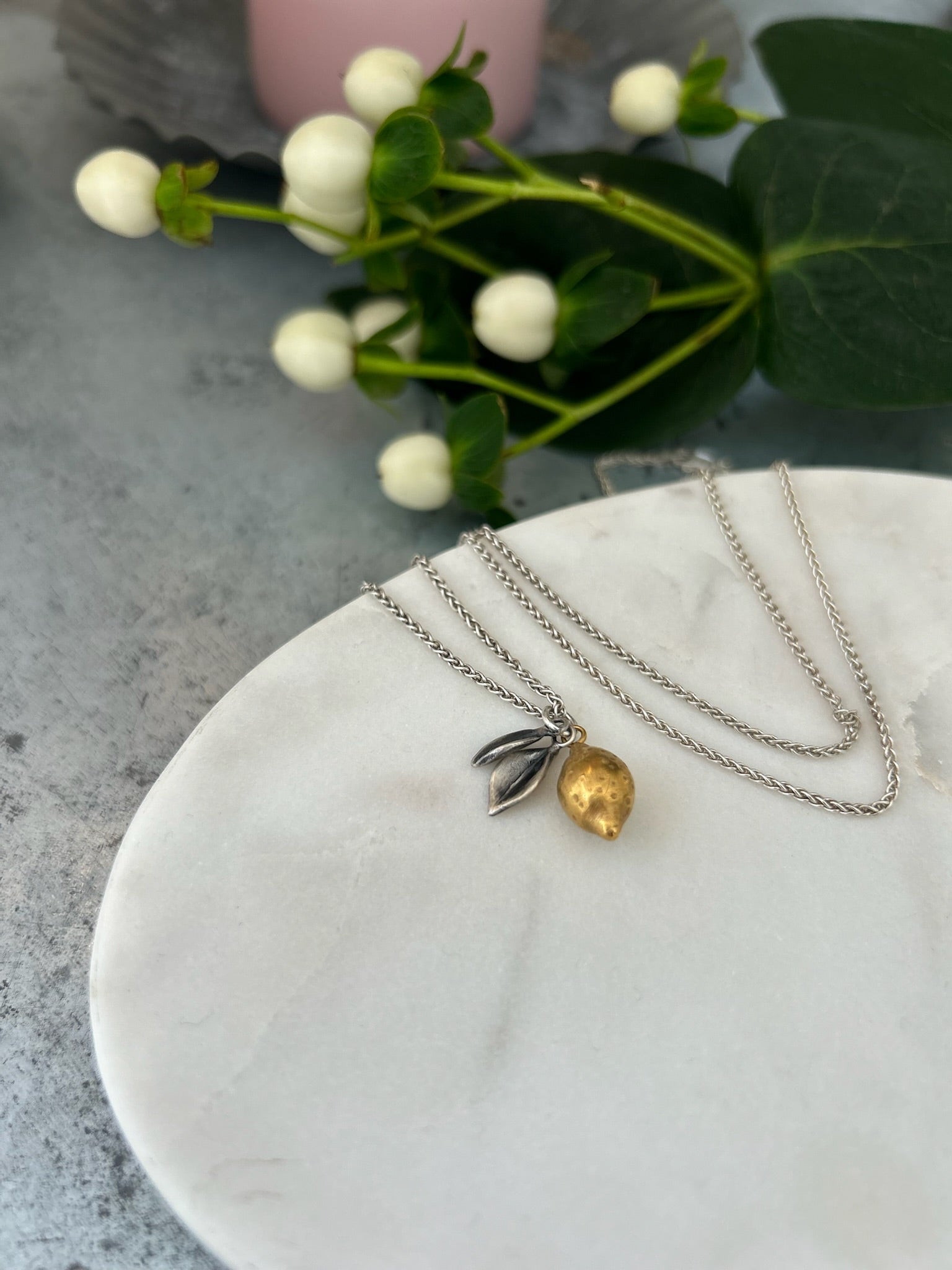 Image shows a Lemon pendant, the lemon is plated in 18ct gold with oxidised silver leaves, hanging from a silver chain.