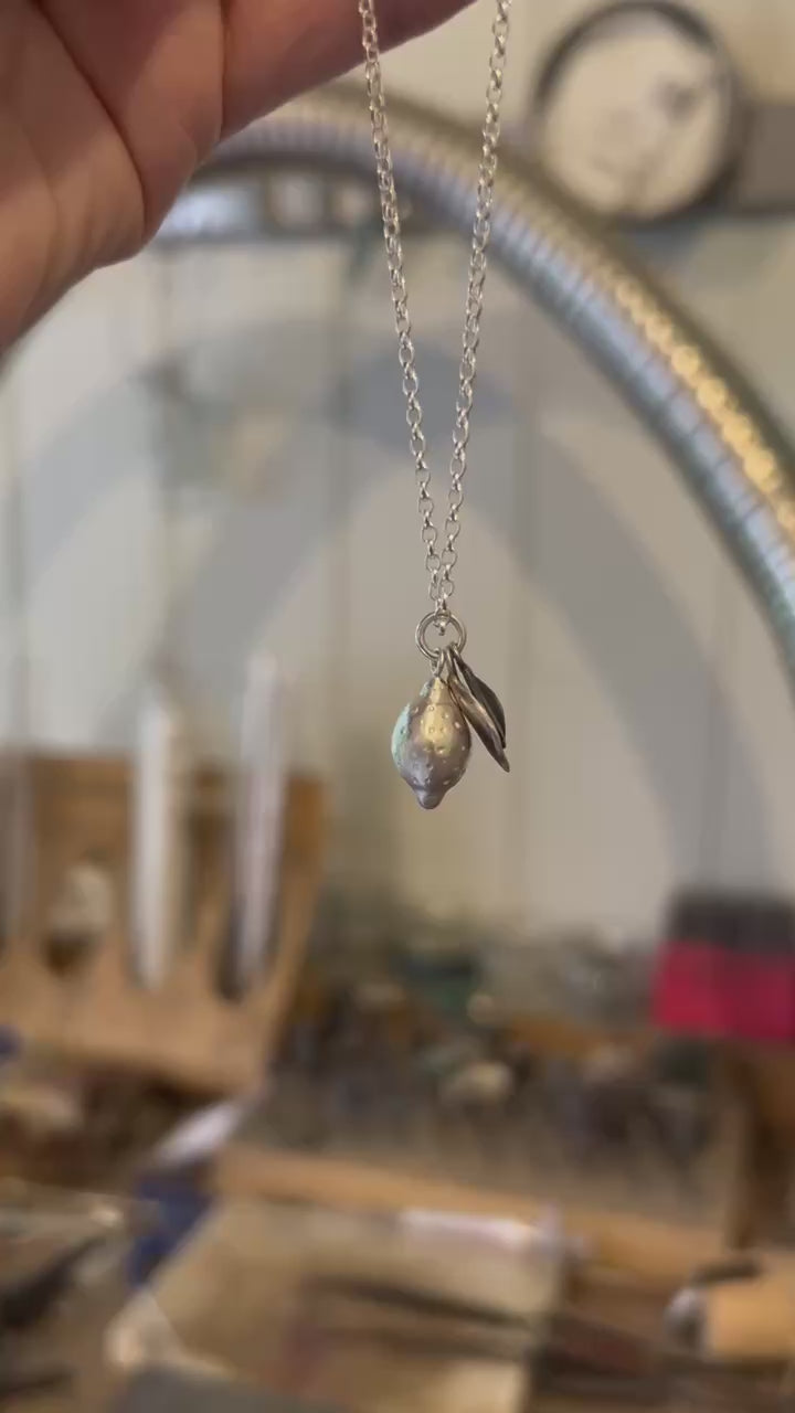 Image shows a Lemon pendant, the lemon has been handcrafted from sterling silver and sits among two silver leaves, hanging from a silver chain.